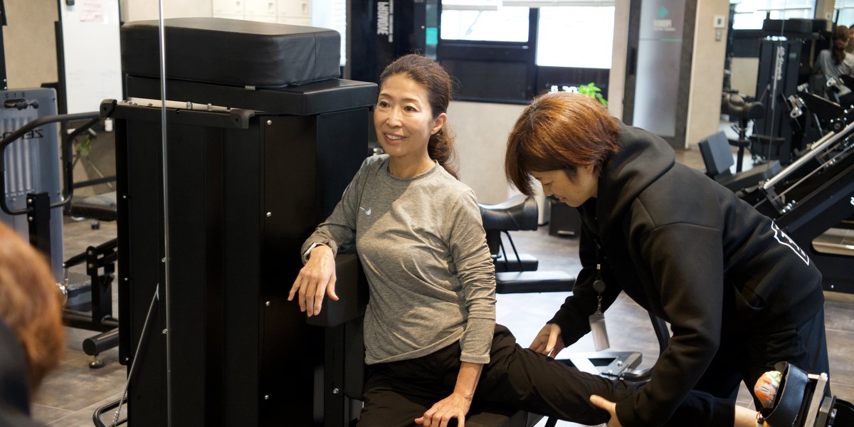 会員様が 4D ストレッチマシンで脚を動かし、トレーナーが横で支えている